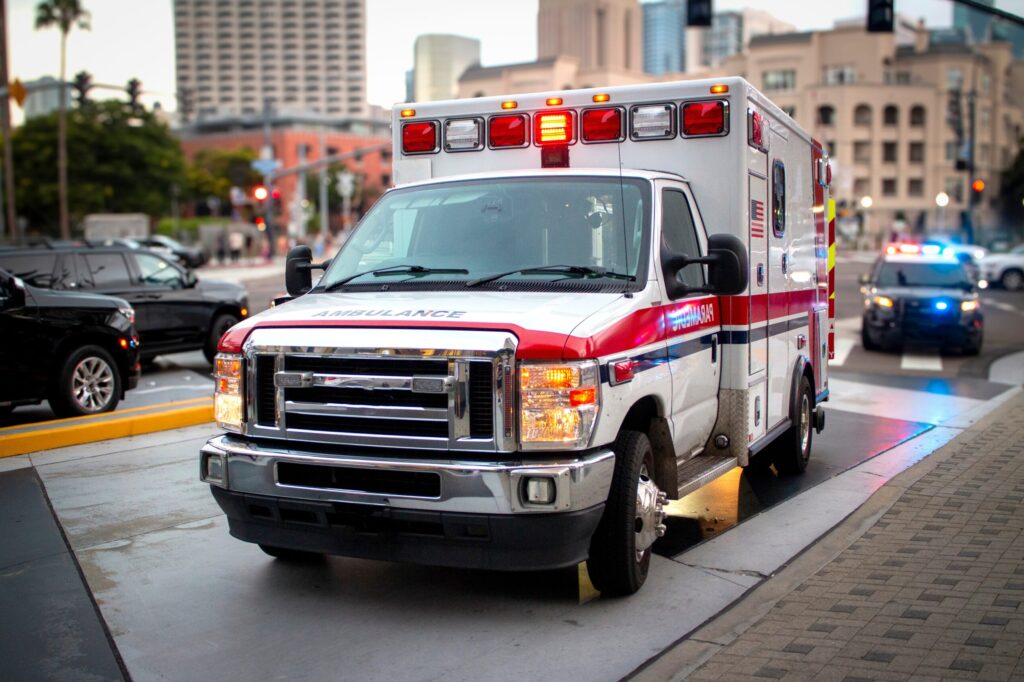 An ambulance with lights activated and a police car behind it parked on a city street in California to pick up a personal injury victim