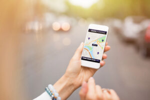 woman holding smartphone with rideshare application of Uber or Lyft open waiting to be picked up, making the rideshare driver and rideshare company liable for damages if a car accident occurs