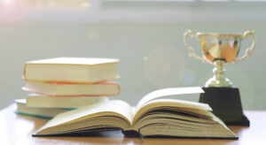 open book under a ray of light next to a trophy to symbolize academic achievements and a scholarship award