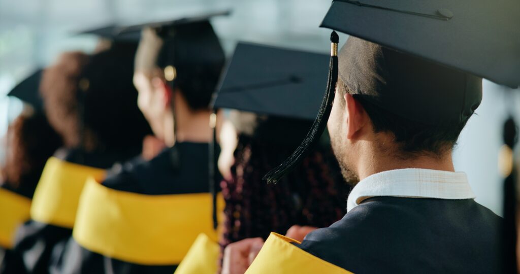 backshot view of students siting during a graduation ceremony, while wearing their cap and gowns