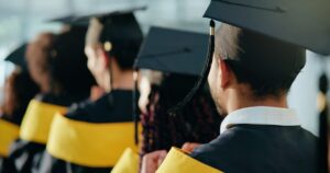 backshot view of students siting during a graduation ceremony, while wearing their cap and gowns