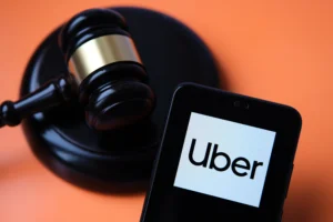 Image of the Uber app pulled up on a phone next to a gavel to represent the new Uber laws and how it will affect injured Uber accdient victims' rights