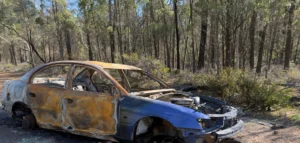 A wrecked car parked in the woods and that was set ablaze and damaged after an incident.