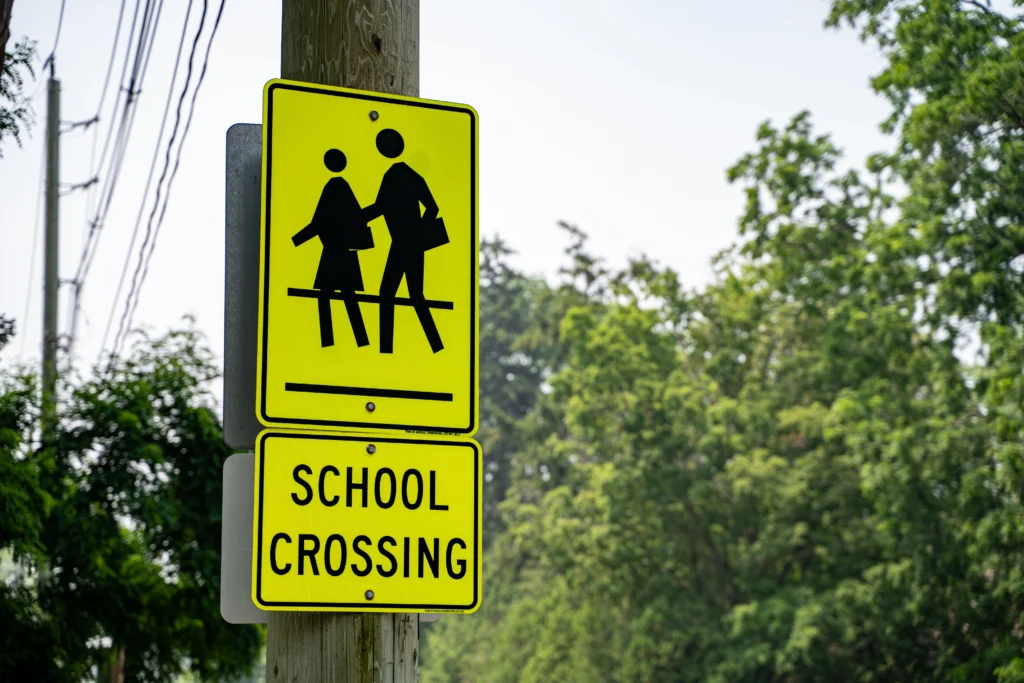 School crossing sign near a local school to warn drivers of approaching foot traffic and to slow their vehicle speed to prevent a car accident that could result in a wrongful death case.